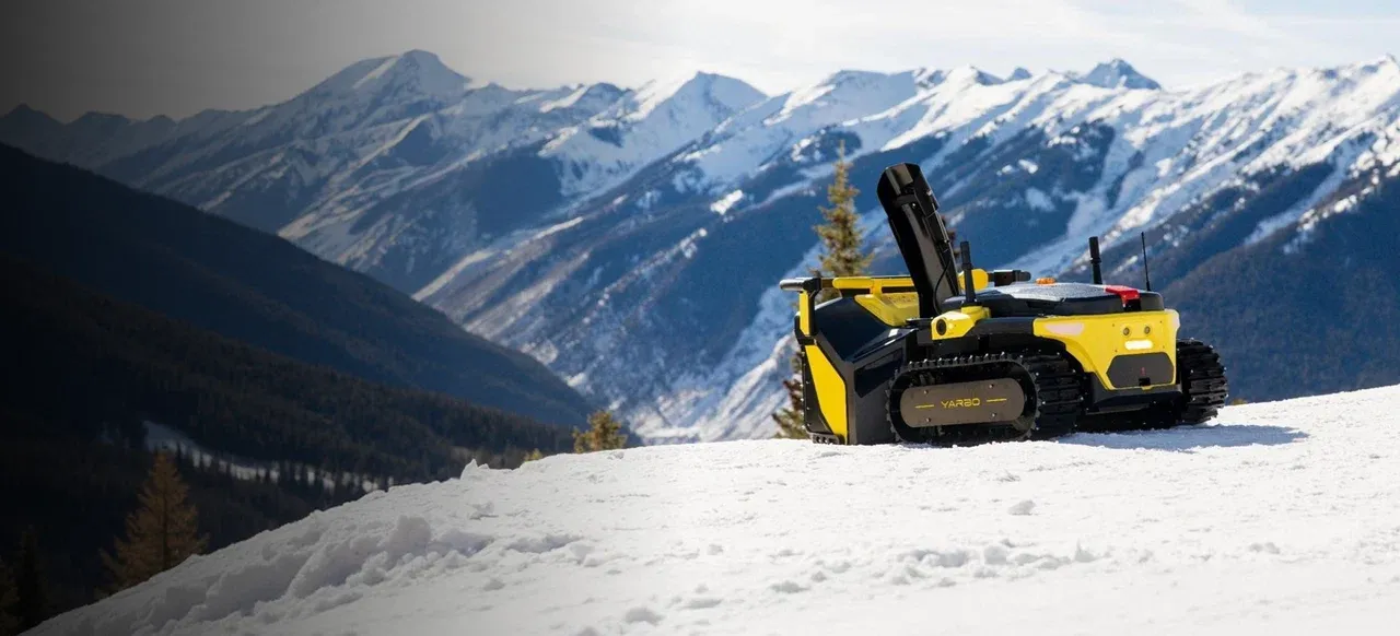 The Yarbo robot parked on a snowy ridge with mountain peaks behind it